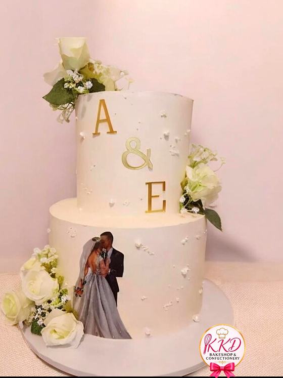 Two tier white wedding cake with gold monogram letters and fresh roses